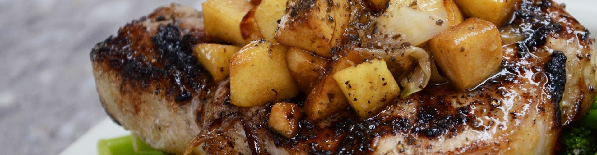 Close up of a rich pork chop topped with cubed roasted potatoes, onion and gravy
