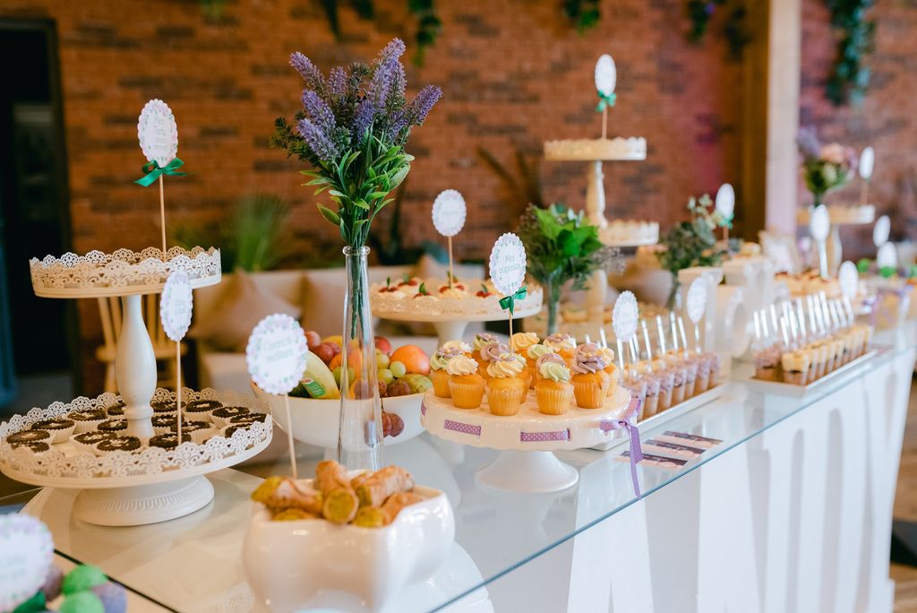 A wedding buffet spread laid out on a white table with purple flowers and food labels